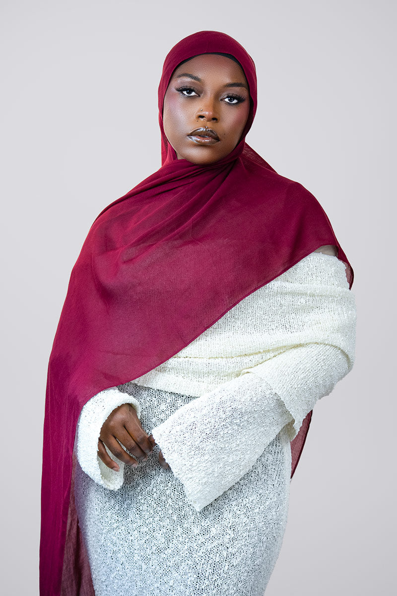 Woman wearing a burgandy modal  hijab and white outfit against a plain background