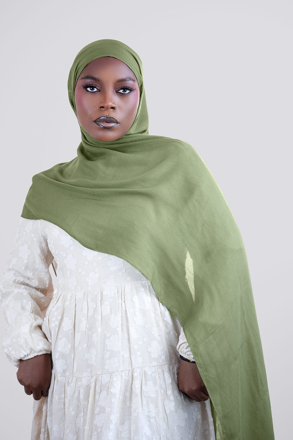 Woman wearing a green hijab and white dress against a plain background
