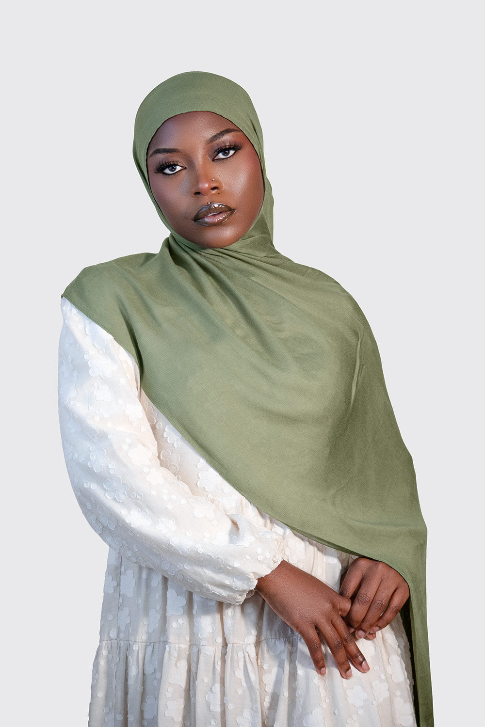 Woman wearing a olive modal  hijab and white outfit on a light gray background