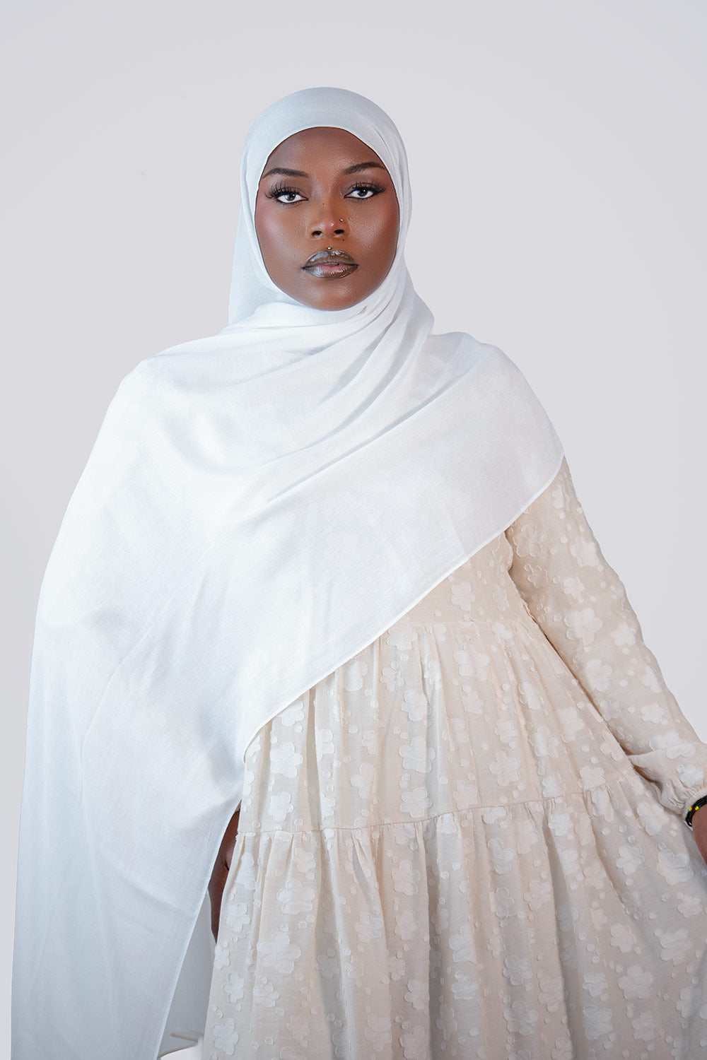 Woman wearing a white hijab and beige dress against a plain background