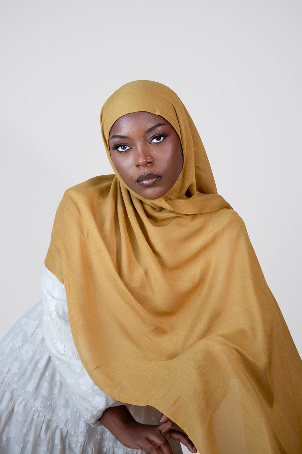 Woman wearing a mustard modal hijab against a plain background