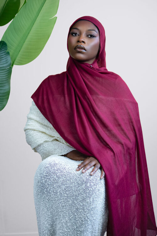 Woman wearing a red hijab and white outfit against a light background