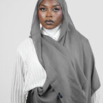 Woman wearing a gray hijab and white shirt on a plain background