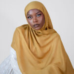 Woman wearing a mustard hijab against a plain background